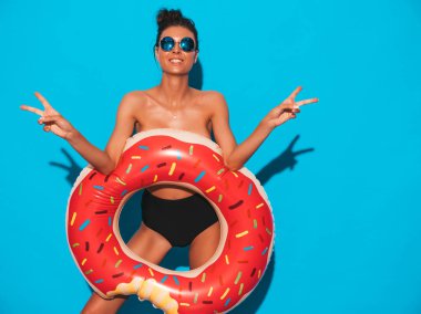 Güneş gözlüğü genç güzel seksi gülümseyen hipster kadın. Yazlık mayo giyen kız. Donut lilo şişme yatak ile göğsünü kapatır. Kadın deliriyordu. Mavi duvarın yanında poz vermek. Barış işaretini gösterir