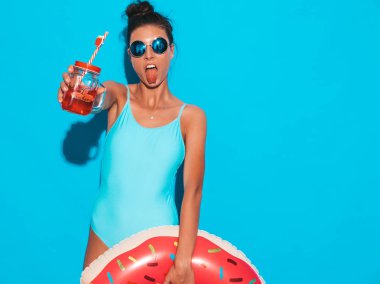 Güneş gözlüğü genç güzel seksi gülümseyen hipster kadın. Donut lilo şişme yatak ile yaz mayo mayo Kız. Mavi duvarın yakınında poz vermek, taze kokteyl içen smoozy içecek
