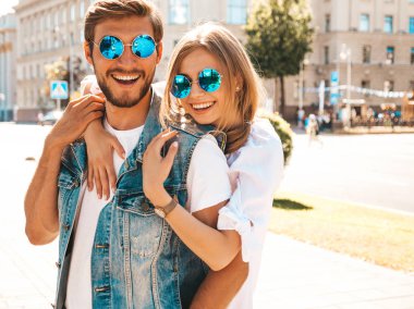 Gülümseyen güzel kız ve yakışıklı erkek arkadaşı. Gündelik yazlık elbiseli kadın ve kot elbiseli adam. Mutlu, neşeli bir aile. Kadın arka planda eğleniyor. Güneş gözlüklü çifte sarılıyor.