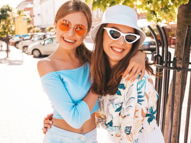 Trendy yazlık giysiler ve panama şapka iki genç güzel gülümseyen hipster kız. Seksi kaygısız kadınlar sokak arka planda poz. Güneş gözlüğü ile eğlenen pozitif modeller. Sarılma