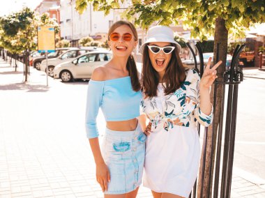 Trendy yazlık giysiler ve panama şapka iki genç güzel gülümseyen hipster kız. Seksi kaygısız kadınlar sokak arka planda poz. Güneş gözlüğü ile eğlenen pozitif modeller. Barış işaretini gösterir
