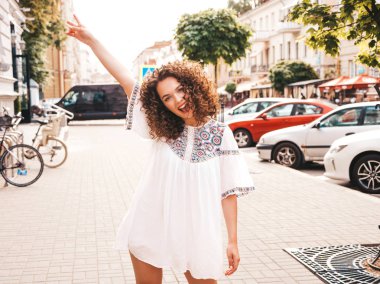 Yaz hipster beyaz elbise giymiş afro bukleler saç modeli ile güzel gülümseyen model portresi. Seksi kaygısız kız sokak arka planda poz. Trendy kadın barış işareti ile el kaldırma