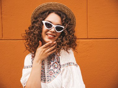 Yaz hipster beyaz elbise ve güneş gözlüğü giymiş afro bukleler saç modeli ile güzel gülümseyen model. Tasasız kız şapkasarı duvar a yakın sokakta poz. Komik ve pozitif kadın eğleniyor