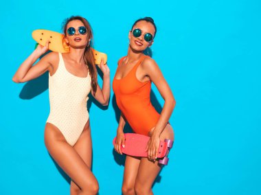 Yaz renkli mayo mayo iki güzel seksi gülümseyen hipster kadın. Güneş gözlüğü trendy Girls. Renkli kuruş kaykaylar ile eğlenen pozitif modeller. Mavi üzerine izole