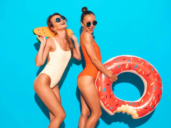 夏のカラフルな水着水着で2美しいセクシーな笑顔ヒップスターの女性 サングラスをかけた女の子カラフルなペニースケートボードを楽しむポジティブなモデル ドーナツリロインフレータブルマットレス付き — ストック写真