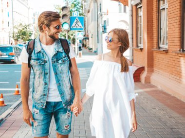 Gülümseyen güzel kız ve yakışıklı erkek arkadaşı. Gündelik yazlık elbiseli kadın ve kot elbiseli adam. Mutlu, neşeli bir aile. Kadın arka planda eğleniyor. Güneş gözlüklü çifte sarılıyor.