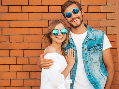 Gülümseyen güzel kız ve onun yakışıklı erkek arkadaşı. Rahat yazlık elbiseli kadın. Kot pantolon giyen adam. Mutlu neşeli bir aile. Kadın tuğla duvara yakın sokakta eğleniyor. Güneş gözlüğü sarılma çift