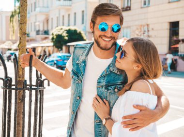 Gülümseyen güzel kız ve onun yakışıklı erkek arkadaşı sokakta poz. Rahat yazlık elbiseli kadın ve kot pantolon giyen bir erkek. Mutlu neşeli çift aile güneş gözlüğü eğlenmek