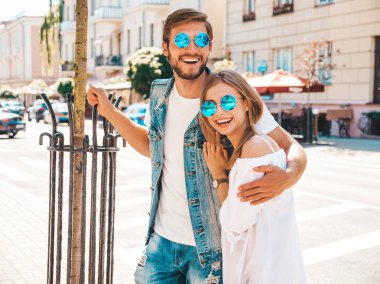 Gülümseyen güzel kız ve onun yakışıklı erkek arkadaşı sokakta poz. Rahat yazlık elbiseli kadın ve kot pantolon giyen bir erkek. Mutlu neşeli çift aile güneş gözlüğü eğlenmek
