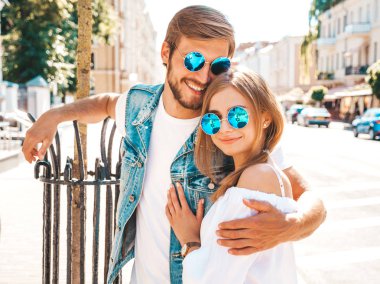 Gülümseyen güzel kız ve onun yakışıklı erkek arkadaşı sokakta poz. Rahat yazlık elbiseli kadın ve kot pantolon giyen bir erkek. Mutlu neşeli çift aile güneş gözlüğü eğlenmek