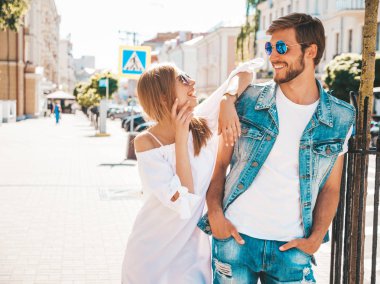 Gülümseyen güzel kız ve onun yakışıklı erkek arkadaşı sokakta poz. Rahat yazlık elbiseli kadın ve kot pantolon giyen bir erkek. Mutlu neşeli çift aile güneş gözlüğü eğlenmek