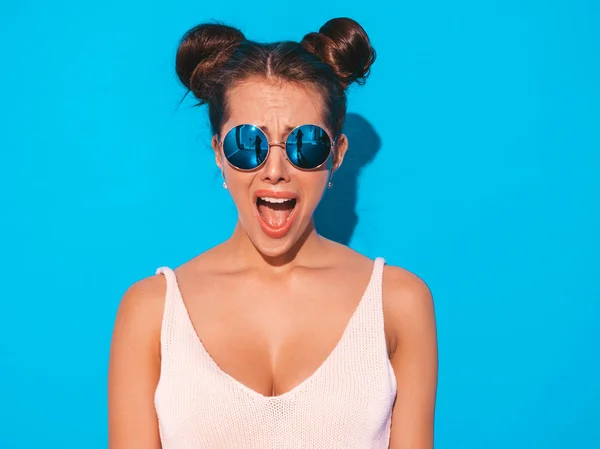 Closeup portrait of young beautiful sexy shocked hipster woman in sunglasses.Trendy Model isolated on blue wall.Shows fear emotion