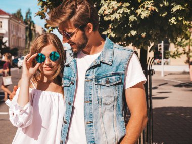 Gülümseyen güzel kız ve yakışıklı erkek arkadaşı. Gündelik yazlık elbiseli kadın ve kot elbiseli adam. Mutlu, neşeli bir aile. Kadın arka planda eğleniyor. Güneş gözlüklü çifte sarılıyor.