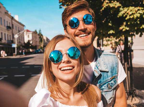 Smiling beautiful girl and her handsome boyfriend in casual summer clothes.Happy family taking selfie self portrait of themselves on smartphone camera in sunglasses.Having fun on the street background