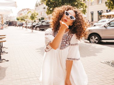 Yaz hipster beyaz elbise giymiş afro bukleler saç modeli ile güzel gülümseyen model. Seksi kaygısız kız sokakta poz. Trendy komik ve pozitif kadın güneş gözlüğü eğlenmek. Hava öpücük verir