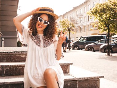 Yaz hipster beyaz elbise giymiş afro bukleler saç modeli ile güzel gülümseyen model. Seksi kaygısız kız sokakta poz. Trendy ve pozitif kadın güneş gözlüğü eğlenmek. Şapkalı. Dili gösterir 