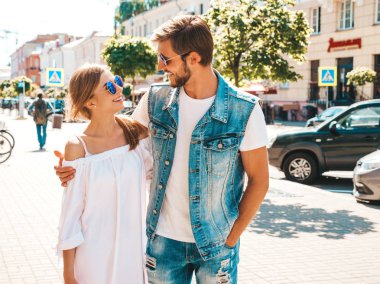 Gülümseyen güzel kız ve yakışıklı erkek arkadaşı. Gündelik yazlık elbiseli kadın ve kot elbiseli adam. Mutlu, neşeli bir aile. Kadın arka planda eğleniyor. Güneş gözlüklü çifte sarılıyor.