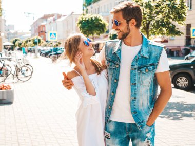 Gülümseyen güzel kız ve yakışıklı erkek arkadaşı. Gündelik yazlık elbiseli kadın ve kot elbiseli adam. Mutlu, neşeli bir aile. Kadın arka planda eğleniyor. Güneş gözlüklü çifte sarılıyor.