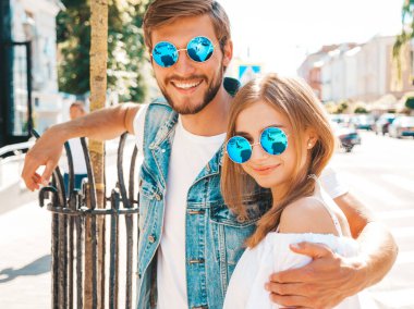 Gülümseyen güzel kız ve yakışıklı erkek arkadaşı. Gündelik yazlık elbiseli kadın ve kot elbiseli adam. Mutlu, neşeli bir aile. Kadın arka planda eğleniyor. Güneş gözlüklü çifte sarılıyor.