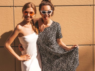 Moda yazlık elbiseler iki genç güzel gülümseyen hipster kız. Seksi kaygısız kadınlar sarı duvarın yakınındaki sokakta poz. Güneş gözlüğü ile eğlenen pozitif modeller