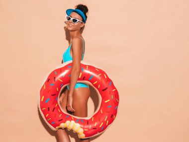 Güneş gözlüğü genç güzel seksi gülümseyen hipster kadın. Donut lilo şişme yatak ile yaz mayo mayo Kız. Pozitif kadın deliriyordu. Şeffaf vizör kapağı bej duvar ayakın