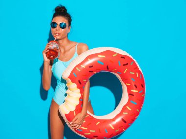 Güneş gözlüğü genç güzel seksi gülümseyen hipster kadın. Donut lilo şişme yatak ile yaz mayo mayo Kız. Mavi duvarın yanında poz vermek. İçme taze kokteyl smoozy içecek