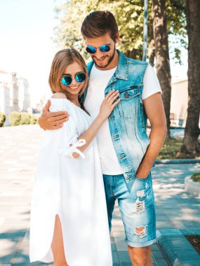 Gülümseyen güzel kız ve yakışıklı erkek arkadaşı. Gündelik yazlık elbiseli kadın ve kot elbiseli adam. Mutlu, neşeli bir aile. Kadın arka planda eğleniyor. Güneş gözlüklü çifte sarılıyor.