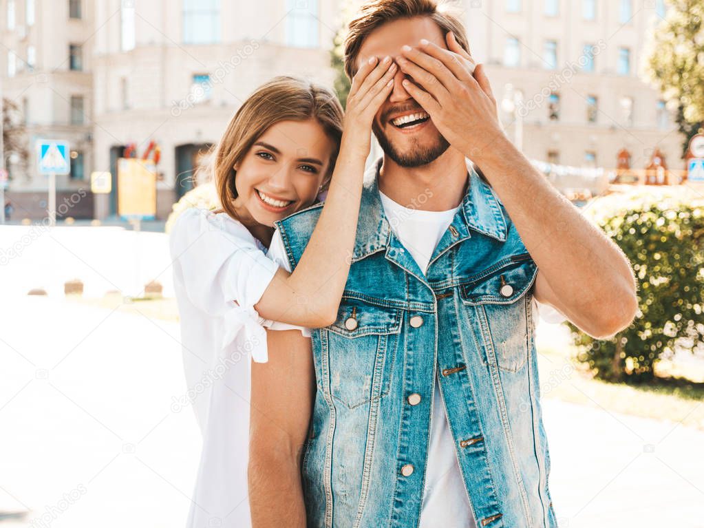 Smiling beautiful girl and her handsome hipster boyfriend. Woman covering her man eyes with hands. Happy cheerful family. Hugging loving couple standing outdoors.Guess who concept 