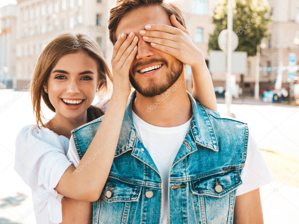 Smiling beautiful girl and her handsome hipster boyfriend. Woman covering her man eyes with hands. Happy cheerful family. Hugging loving couple standing outdoors.Guess who concept 