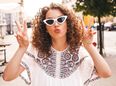 Yaz hipster beyaz elbise giymiş afro bukleler saç modeli ile güzel gülümseyen model. Seksi kaygısız kız sokakta poz. Trendy komik ve pozitif kadın güneş gözlüğü eğlenmek. Barış işaretini gösterir