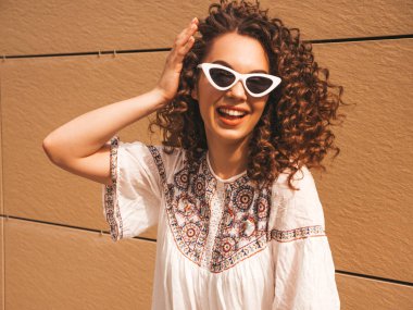 Yaz hipster beyaz elbise ve güneş gözlüğü giymiş afro bukleler saç modeli ile güzel gülümseyen model. Seksi kaygısız kız sarı duvara yakın sokakta poz. Komik ve pozitif kadın eğleniyor