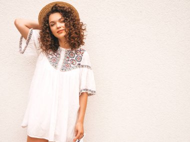 Yaz hipster beyaz elbise giymiş afro bukleler saç modeli ile güzel gülümseyen model. Seksi kaygısız kız şapka beyaz duvar yakınında sokakta poz. Komik, pozitif kadın eğleniyor ve delioluyor