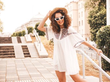 Yaz hipster beyaz elbise giymiş Afro bukleler saç ile güzel gülümseyen model. Seksi kaygısız kız sokakta poz. Şık komik ve pozitif kadın güneş gözlüğü ve şapka eğlenmek