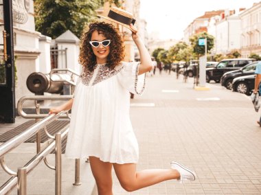 Yaz hipster beyaz elbise giymiş Afro bukleler saç ile güzel gülümseyen model. Seksi kaygısız kız sokakta poz. Şık komik ve pozitif kadın güneş gözlüğü ve şapka eğlenmek