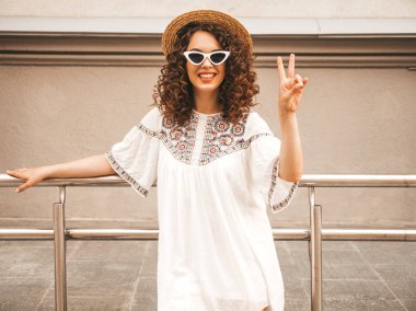 Yaz hipster beyaz elbise giymiş Afro bukleler saç ile güzel gülümseyen model. Seksi kaygısız kız sokakta poz. Pozitif kadın güneş gözlüğü ve şapkalı eğleniyor. Barış işaretini gösterir