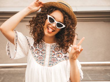 Yaz hipster beyaz elbise giymiş Afro bukleler saç ile güzel gülümseyen model. Seksi kaygısız kız sokakta poz. Pozitif kadın güneş gözlüğü ve şapkalı eğleniyor. Barış işaretini gösterir