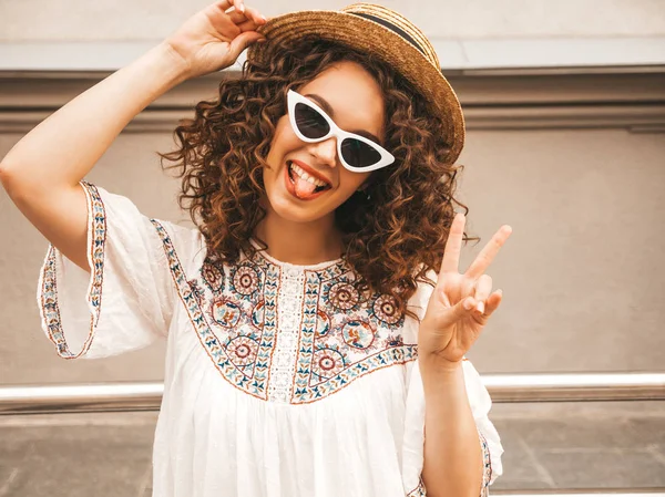Yaz hipster beyaz elbise giymiş Afro bukleler saç ile güzel gülümseyen model. Seksi kaygısız kız sokakta poz. Pozitif kadın güneş gözlüğü ve şapkalı eğleniyor. Barış işaretini gösterir