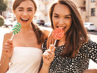 Trendy yaz giysileri iki genç güzel gülümseyen hipster kız. Seksi kaygısız kadınlar sokak arka planda poz. Olumlu modeller eğleniyor. Şeker lolipop yeme