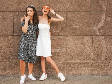 Trendy yaz elbisesi iki genç güzel gülümseyen hipster kız. Seksi kaygısız kadınlar sarı duvarın yakınındaki sokakta poz. Güneş gözlüğü ile eğlenen pozitif modeller.
