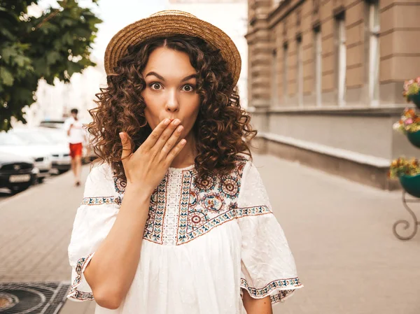 Portrait of beautiful model with afro curls hairstyle dressed in summer hipster white dress.Sexy carefree girl posing in the street background.Trendy woma closing her mouth.Secret consept