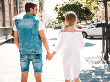 Güzel kızın ve yakışıklı erkek arkadaşının birbirlerinin ellerini tutup, ona baktığının arkası. Rahat yazlık elbiseli kadın ve kot pantolon giymiş bir erkek. Mutlu neşeli aile sokakta poz