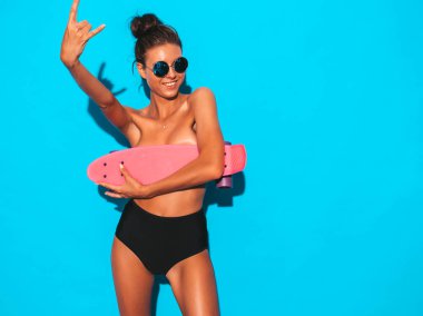 Güneş gözlüğü genç güzel seksi gülümseyen hipster kadın. Yaz mayo mayo moda kız. Pozitif kadın deli gidiyor ve pembe kuruş kaykay ile göğsünü kapsar