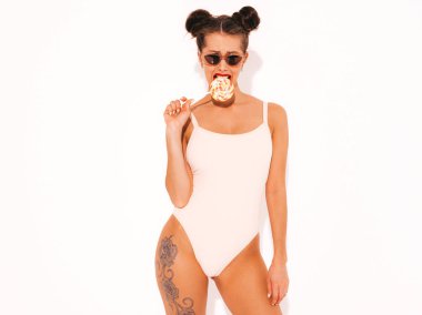 Güneş gözlüğü kırmızı dudaklar ile Genç güzel seksi hipster kadın. Yaz mayo giysileri trendy kız. Pozitif kadın deliriyordu. Komik model beyaz izole. İki boynuz. Yeme, ısırma şeker lolipop