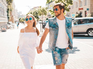 Gülümseyen güzel kız ve onun yakışıklı erkek arkadaşı sokakta poz. Rahat yazlık elbiseli kadın ve kot pantolon giyen bir erkek. Mutlu neşeli çift aile güneş gözlüğü eğlenmek