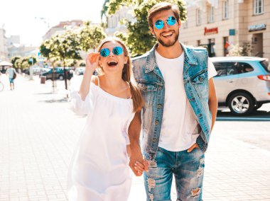Gülümseyen güzel kız ve onun yakışıklı erkek arkadaşı sokakta poz. Rahat yazlık elbiseli kadın ve kot pantolon giyen bir erkek. Mutlu neşeli çift aile güneş gözlüğü eğlenmek