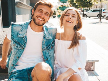 Gülümseyen güzel kız ve onun yakışıklı erkek arkadaşı. Rahat yazlık elbiseli kadın ve kot pantolon giyen bir erkek. Mutlu neşeli bir aile. Sokak arka planında merdivenlerde oturuyorum. Sarılan çift