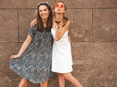 Trendy yaz elbisesi iki genç güzel gülümseyen hipster kız. Seksi kaygısız kadınlar sarı duvarın yakınındaki sokakta poz. Güneş gözlüğü ile eğlenen pozitif modeller. Hava öpücüğü verir. Göz kırpma