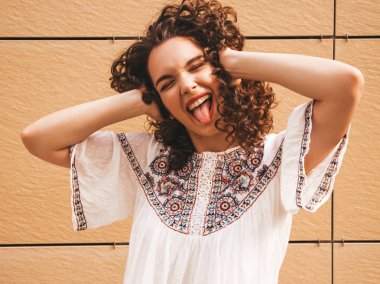 Yaz hipster beyaz elbise giymiş afro bukleler saç modeli ile güzel gülümseyen model. Seksi kaygısız kız sarı duvara yakın sokakta poz. Komik ve pozitif kadın eğleniyor. Dili gösterir. Çığlık