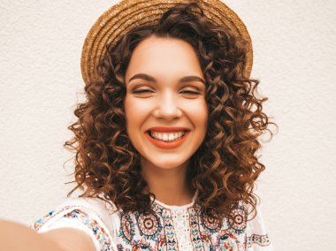 Yaz hipster beyaz elbise giymiş afro bukleler saç modeli ile güzel gülümseyen model. Sokakta poz seksi kaygısız kız. Akıllı telefonda şapkayla selfie selfie portre fotoğrafları çekmek