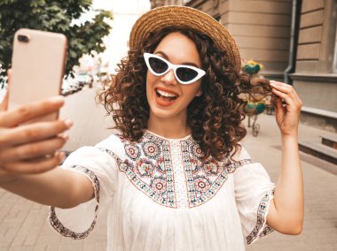 Yaz hipster beyaz elbise giymiş afro bukleler saç modeli ile güzel gülümseyen model. Seksi kaygısız kız güneş gözlüğü sokakta poz. Şapkalı akıllı telefonda selfie selfie portre fotoğrafları çekmek